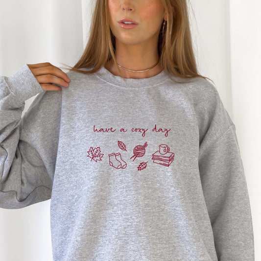 „Have a Cozy Day“ – Herbstliches Design mit geschwungener Schrift und Symbolen wie Blättern, Socken, Büchern und Wolle. Ideal für DIY-Tassen, Kissen und Herbstdeko.